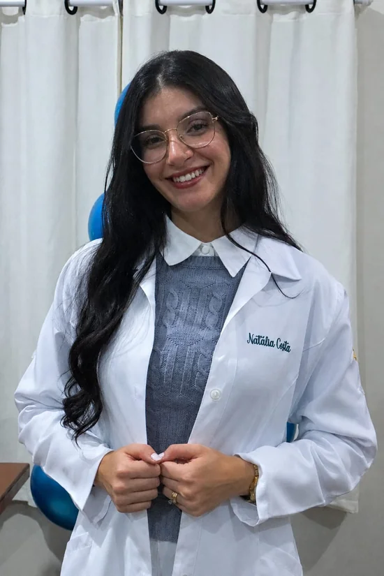Natália Gregorio sorrindo, de jaleco, no consultório